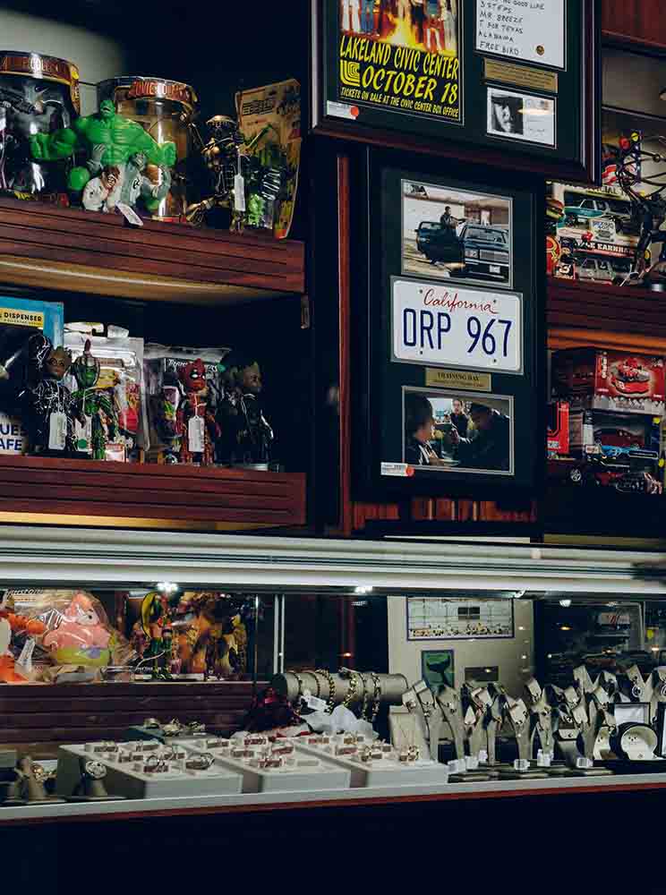 Shelves and a display case in a shop featuring jewelry, toys and a framed Fast & Furious license plate memorabilia piece. .